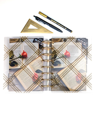 Discbound planner with gold discs, pens, ruler, and decorative books and roses cardstock dashboard with a clear plaid planner cover on a white background
