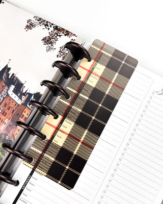 Open Jane’s Agenda discbound planner with dark metallic discs, featuring a black, cream, and red plaid page finder layered over weekly meal-planning and checklist pages, with a castle dashboard visible underneath.