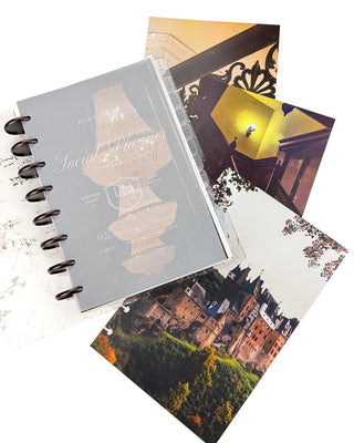 Open Jane’s Agenda discbound planner with dark metallic discs and monthly tabs, featuring a frosted “The Social Planner Club” dashboard layered over a glowing chandelier image, with coordinating staircase, architectural interior, and castle dashboards displayed beside it.