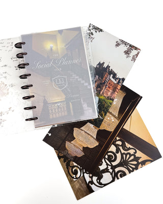 Open Jane’s Agenda discbound planner with dark metallic discs and monthly tabs, featuring a frosted “The Social Planner Club” dashboard layered over a grand staircase image, with coordinating castle, chandelier, and ornate architectural dashboards displayed beside it.