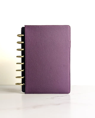 Standing view of closed purple planner with visible gold discs and a textured vegan leather finish.