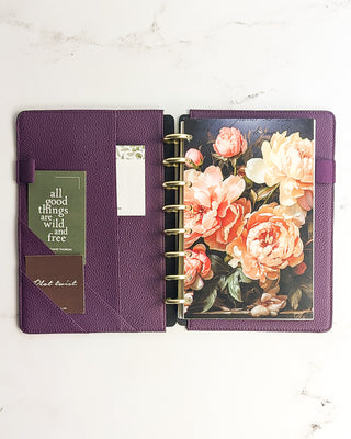 Open purple snap planner cover from Jane's Agenda with gold disc-bound inserts, floral dashboard, and cards stored in angled interior pockets.