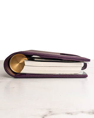 Bottom view of a purple planner wrap cover by Jane's Agenda with a gold disc-bound planner inside, lying on its side with visible stacked pages.