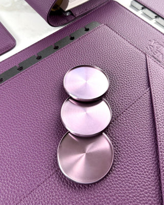 Close-up of a purple leather planner cover with lavender colored metallic binding discs on a white background