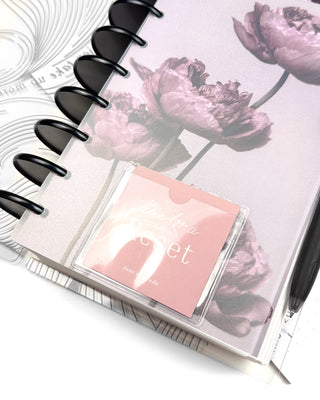 Discbound planner with a soft mauve floral cover and black discs featuring a clear front pocket holding a blush “Time for a Reset” dashboard card. Styled with a black pen and coordinating abstract line dashboard underneath.