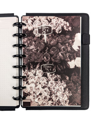Sepia toned photograph of flowers at a market with handwritten price signs, snapped into a planner with Black Plastic Discs and Black Vegan Leather Snap-on Cover on a white background. 