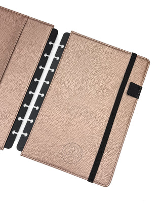 Rose gold leather planner cover for discbound planners, with a black elastic ribbon over a white background.