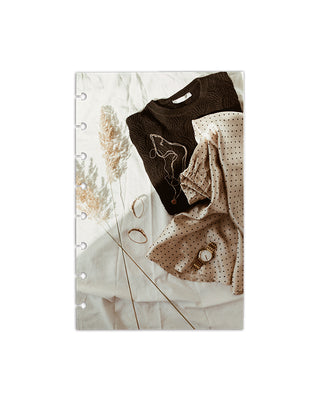 Featuring brown knit sweater, cream skit with black polk-a-dots, and gold jewelry laid out on soft white linens printed on a dashboard over a white background. 