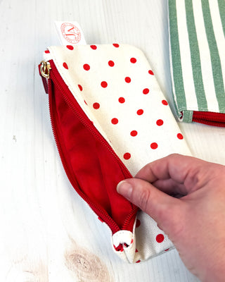 Small fabric pouch with red and cream polka dot pattern and red zipper closure displaying interior compartment