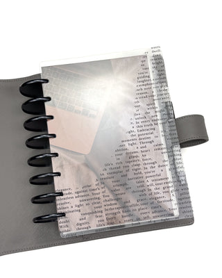 Planner with a clear cover, and a laptop and pen ona discbound planner dashboard in a disc planner system, over a white background.