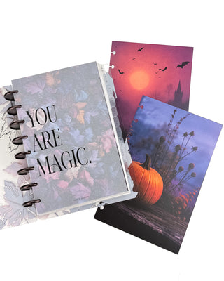 Open Jane’s Agenda discbound planner with dark metallic discs and monthly side tabs, featuring a frosted “YOU ARE MAGIC.” dashboard layered over colorful autumn leaves, alongside coordinating Halloween dashboards with a glowing moon, flying bats, and a pumpkin scene.