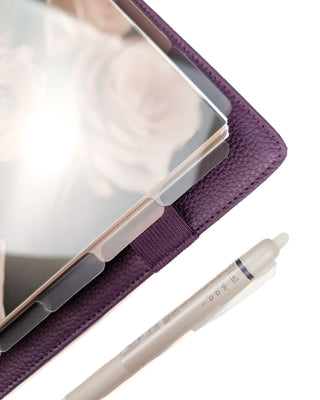 Close up image of a purple discbound planner with a set of stained glass-like plastic planner dividers that are multi-colored and translucent all on a white background.