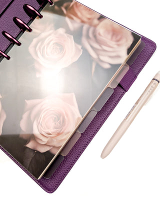 Purple discbound planner on purple binding discs with a set of six stained glass-like plastic planner dividers that are multi-colored and translucent all on a white background.