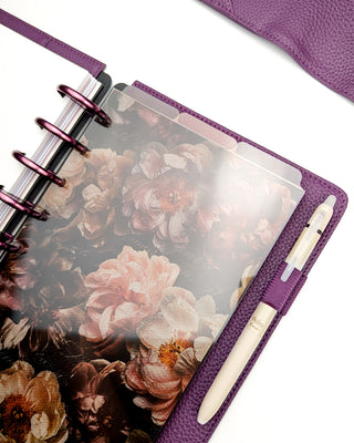A set of three stained glass translucent multi-color top tabbed plastic planner dividers placed in a purple discbound planner with purple discs and a beige pen over a white background