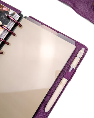 A set of three stained glass translucent multi-color top tabbed plastic planner dividers placed in a purple discbound planner with purple discs and a beige pen over a white background