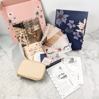 Floral-themed stationery set including notebooks, a pouch, and planner sheets on a marble surface.