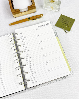 An open discbound planner with a 'Passwords' page on a white surface with a pen and a small box.