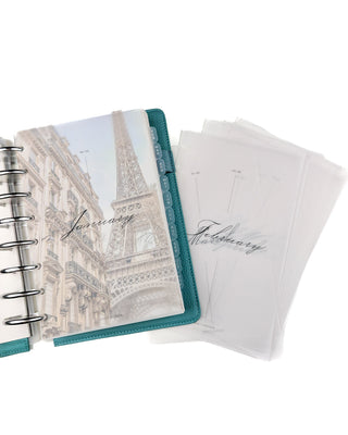 Open discbound planner withsilver metal binding discs with an Eiffel Tower designed planner dashboard andTwelve sheets of frosted vellum paper with black cursive font depicting each month of the year on a white background