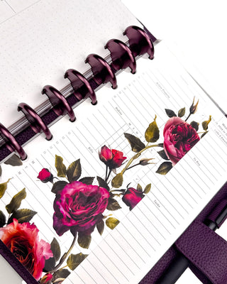 Featuring victorian-inspired vibrant rose glass clear plastic hybrid dashboard snapped onto a disc-bound planner. With Violet purple binding discs with a purple vegan leather wrap around cover on a white background. 