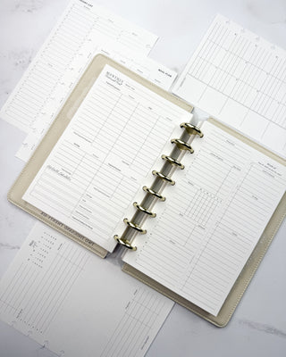 Jane's Agenda discbound planner open to a monthly budget insert, with weekly planner inserts, meal plan, grocery list, and monthly inserts around a cream vegan leather planner cover with gold Metal Binding Discs.