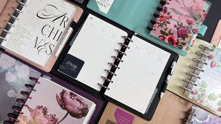 Collection of colorful discbound planners with calendar pages, and floral designs on a neutral background
