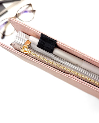 Close-up of a closed planner featuring a taupe brown zipper pouch with gold metal zipper and pull, and a Waai Pilot FriXion pen in the pen loop, on a white background.