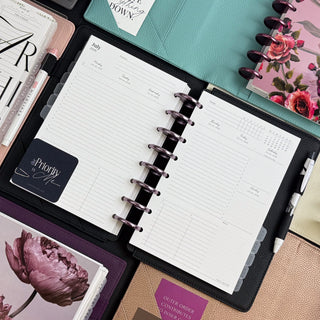 Jane's Agenda Discbound Planner System flatlay – open weekly Planner Inserts with Metal Binding Discs, black Planner Cover, Tabbed Dividers, and multiple Planner Covers in teal, floral, and purple.